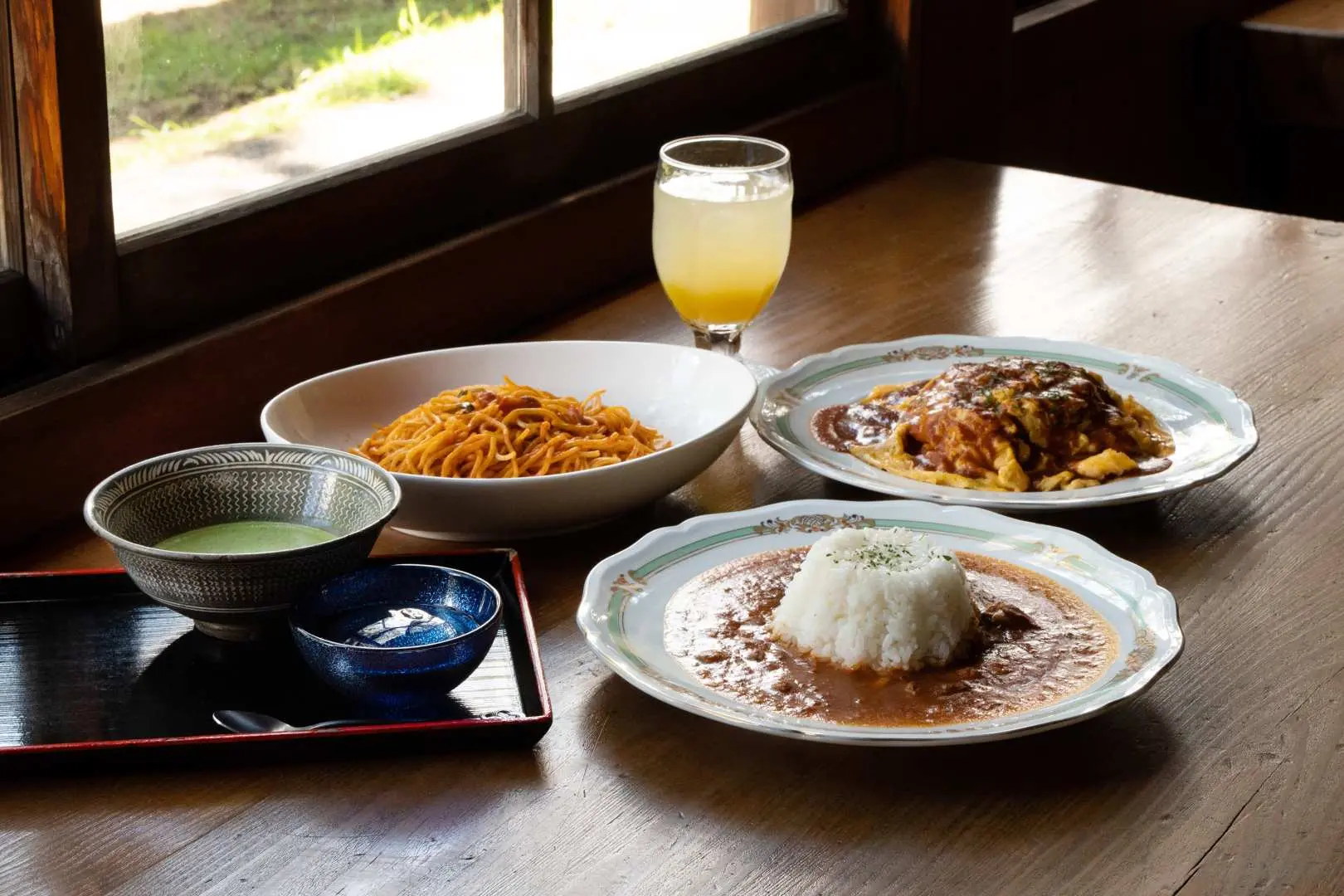 A close-up of Café Shuuma's lunch at Numazu Imperial Villa, featuring their signature curry, various main dishes, and beverages, highlighting the park's unique seasonal menu and exquisite flavors inspired by imperial recipes.