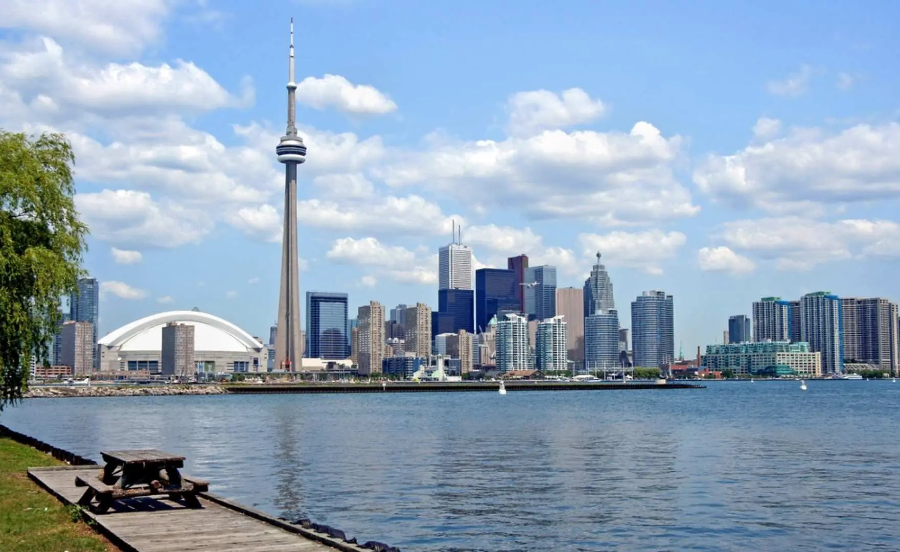 During a Toronto day tour, admire the downtown Toronto skyline from Lake Ontario in the daytime, featuring the majestic CN Tower and Rogers Centre.