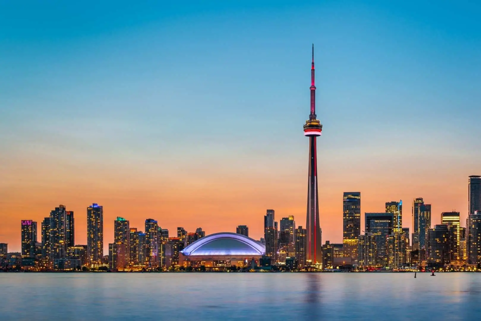 After a Toronto day tour, gaze upon the dazzling Toronto city night view from Lake Ontario at dusk, with the illuminated CN Tower and skyline.