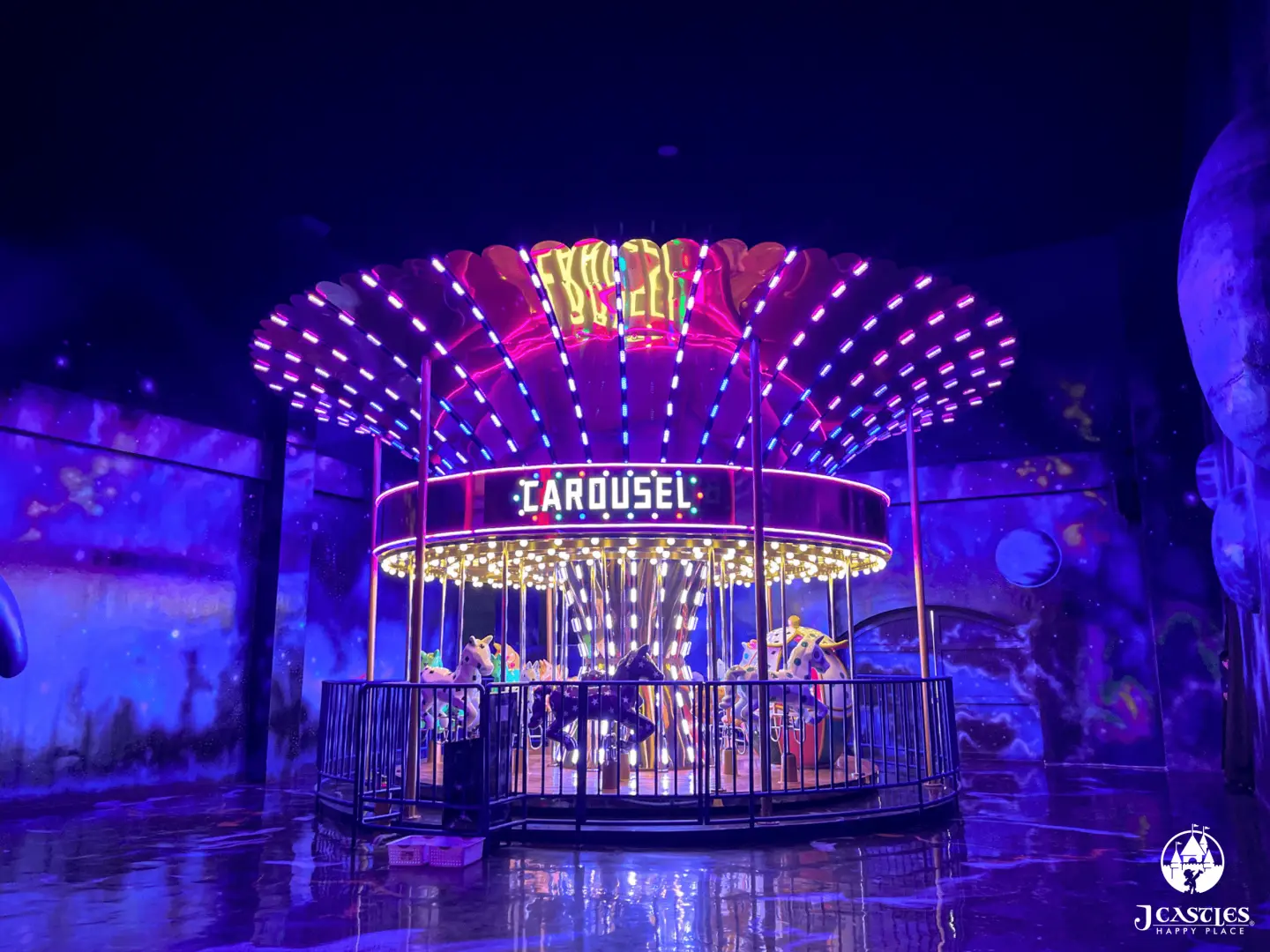 The dazzling indoor carousel at JCastles' Castle Carnival, illuminated with vibrant purple and pink LED lights amidst a celestial-themed backdrop, offering a magical ride experience.