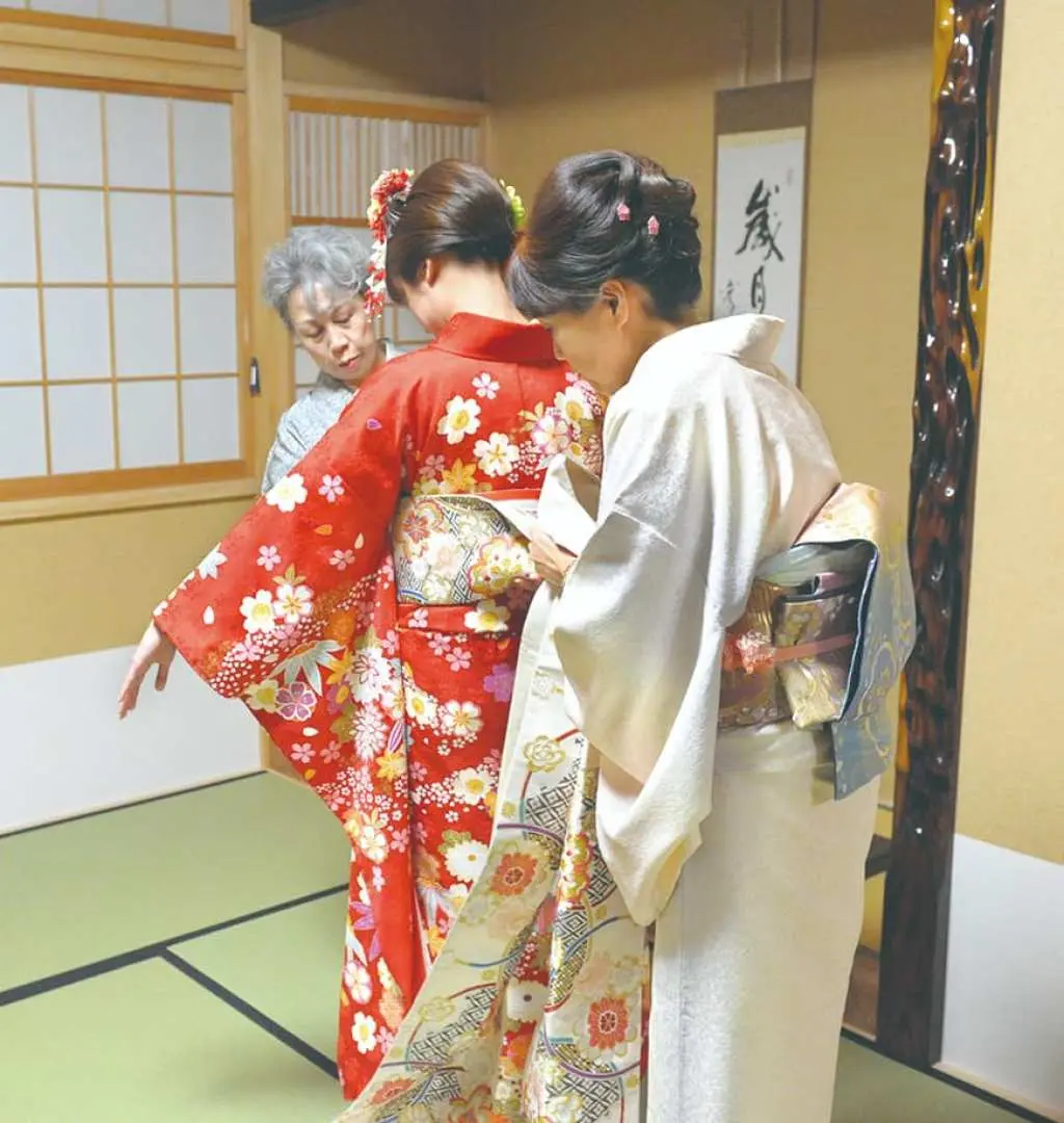 A guest receives attentive assistance from staff to wear a beautiful kimono in a traditional Japanese room in Kisarazu, Chiba, preparing for a photoshoot.