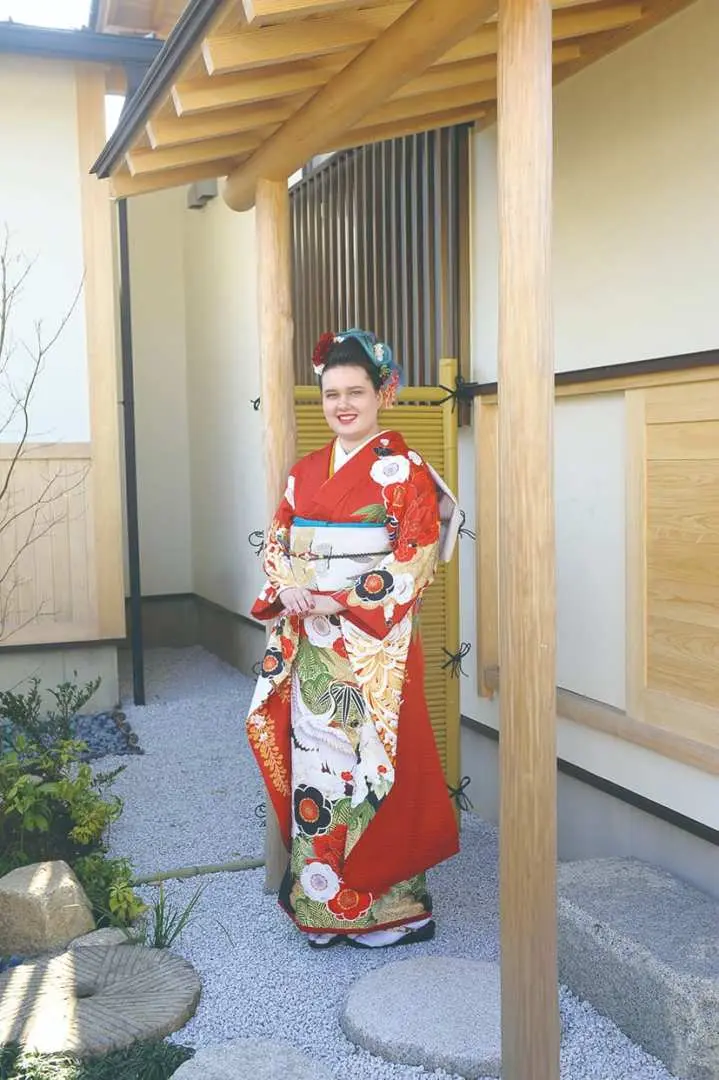 A lady in a vibrant red traditional kimono showcased at the entrance of a Japanese garden in Kisarazu, Chiba, highlighting beautiful patterns for photography.