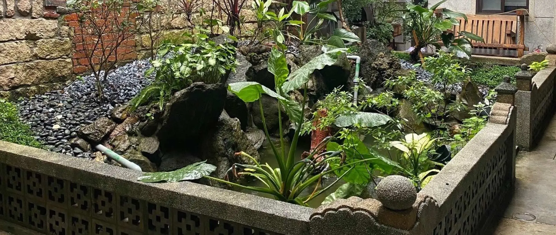 A serene inner courtyard at Yeh Jihn Fa Rice Mill in Taipei's Dihua Street, featuring a beautifully landscaped pond with lush greenery, offering a peaceful escape within the historic site.
