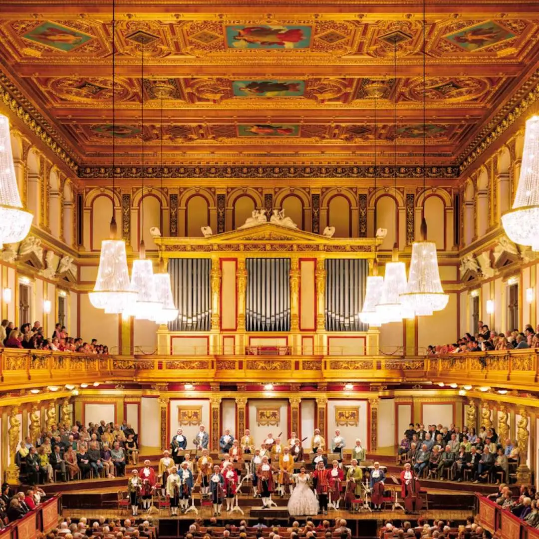 The opulent interior of Vienna's Golden Hall or State Opera House, where an audience enjoys the Mozart Orchestra performing on a grand stage, offering a premier Austrian music experience.