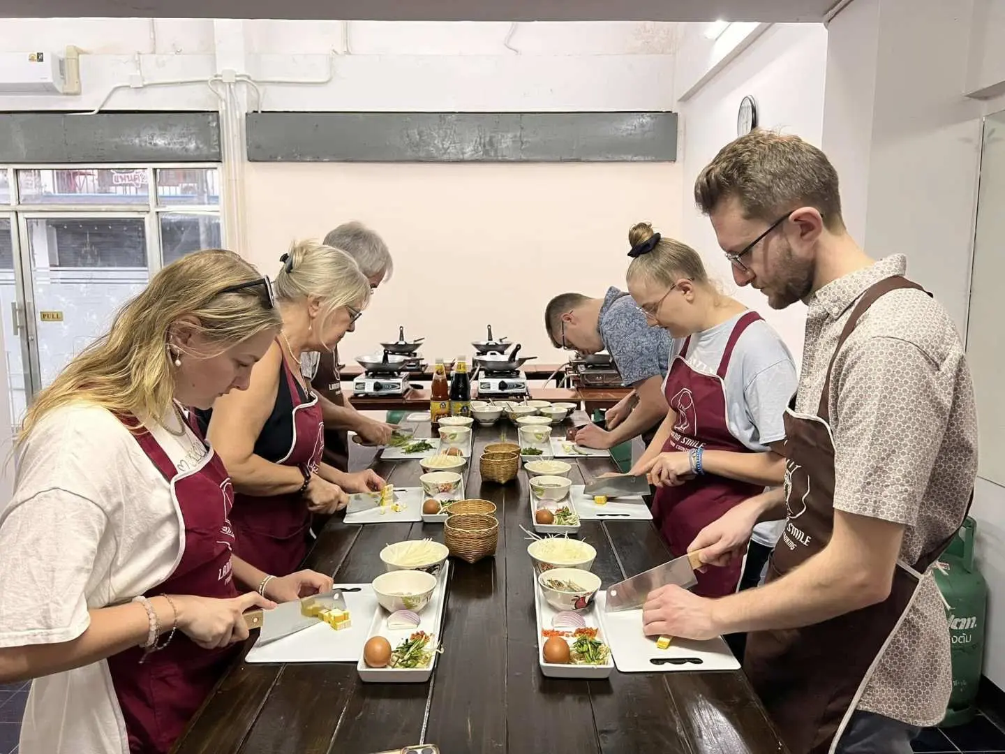 Engaged participants diligently chopping fresh vegetables and ingredients at their individual stations during a hands-on Lanna Smile Thai cooking class in Chiang Mai.