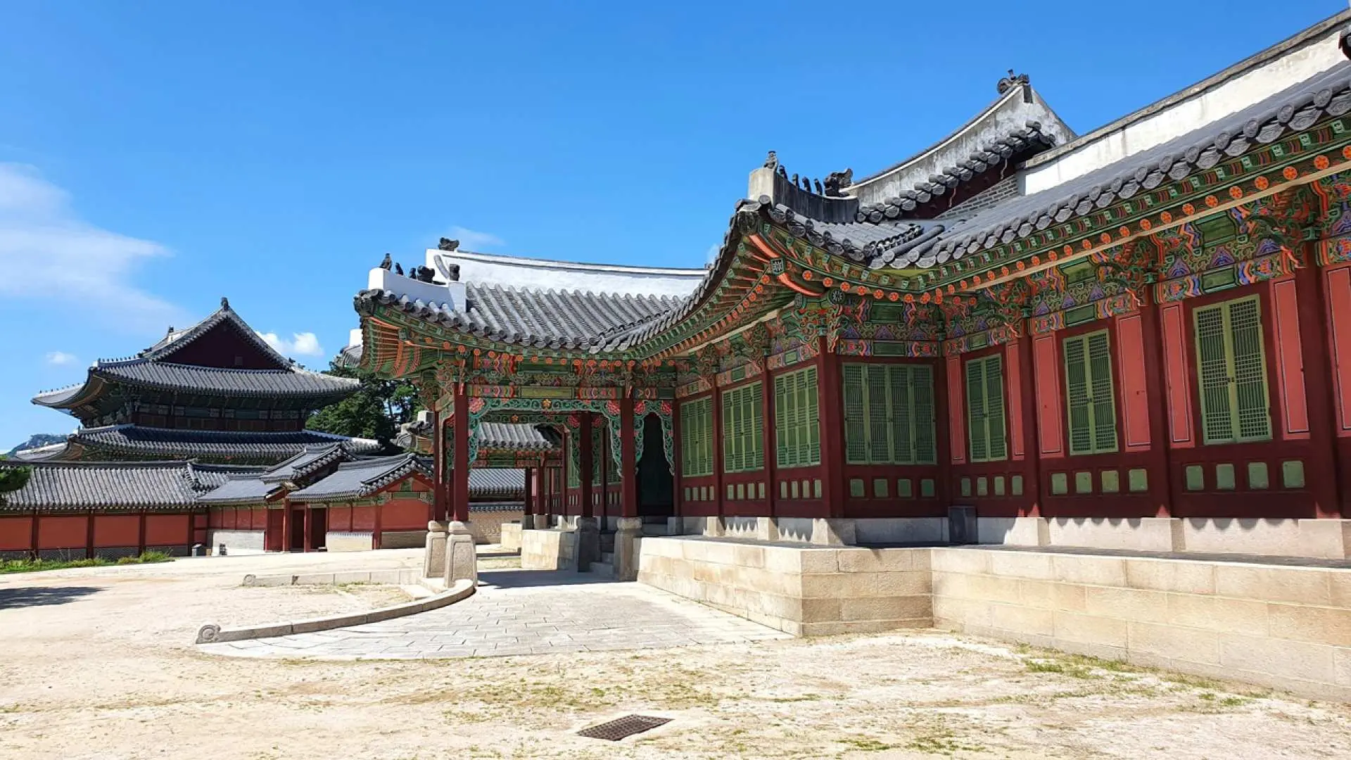 首尔昌德宫宏伟的宫殿建筑群在蓝天下，色彩斑斓的屋檐与静谧的庭院展现韩国历史风华。
