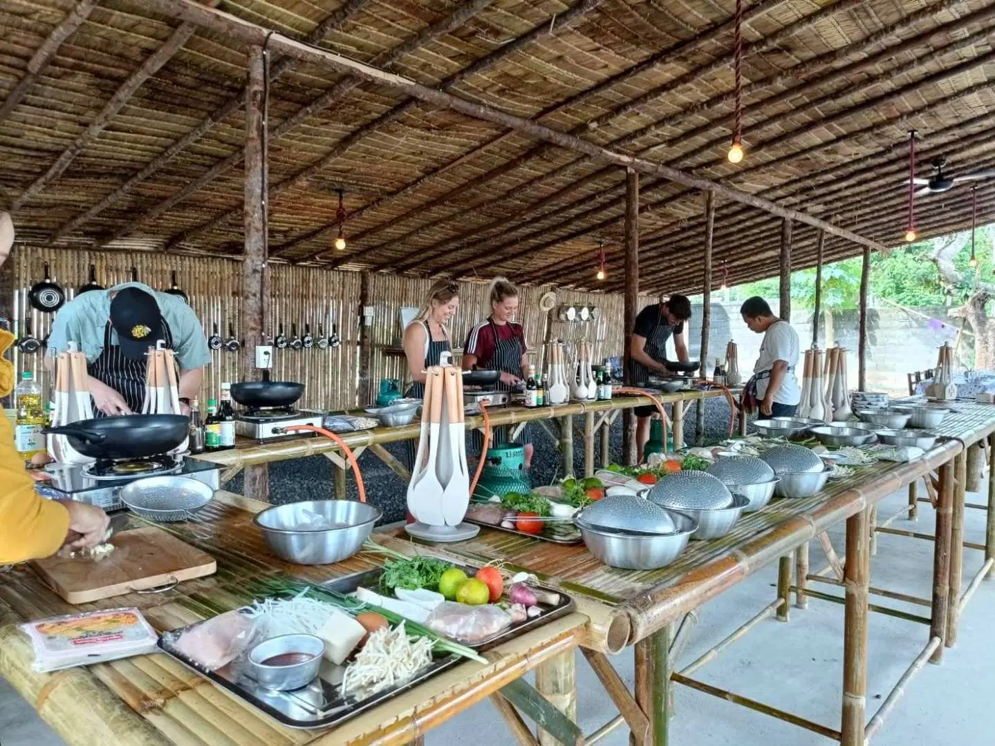 苏梅岛泰式烹饪课上，一群学员在宽敞的露天传统厨房里，用新鲜食材在各自的烹饪台前积极动手制作美食。