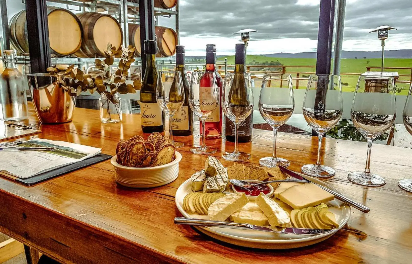 An elegant wine tasting setup at a Yarra Valley winery, featuring selected wines, gourmet cheese, and crackers with barrels in the background.
