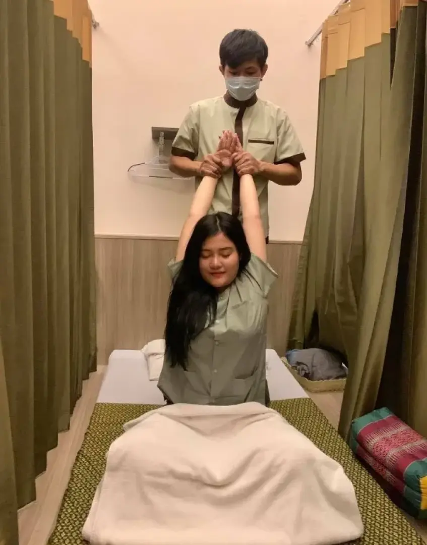 A Thai masseuse performing a traditional Thai massage, stretching a client's arms, showcasing the therapeutic and relaxing spa experience available in Phuket.