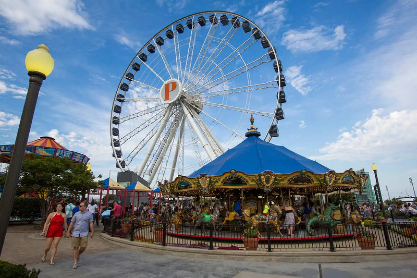 Visitors at Chicago's Navy Pier admire the Centennial Wheel and carousel, experiencing the famous lakeside amusement with the Explorer Pass for ultimate fun.