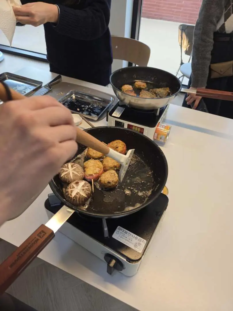 Đôi tay cẩn thận nấu nhiều loại bánh jeon Hàn Quốc, bao gồm bánh nấm và bí ngòi, trong chảo trong lớp học nấu ăn thực hành do đầu bếp Michelin hướng dẫn tại Seoul.