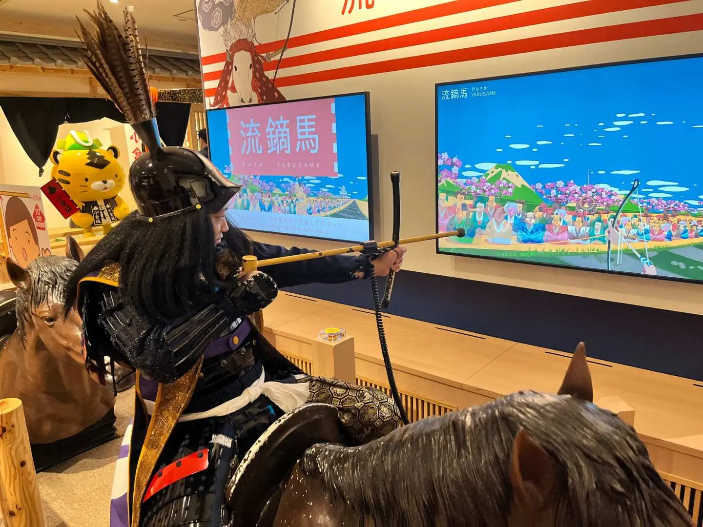 遊客在福岡小倉城體驗流鏑馬射箭互動遊戲，身穿武士服裝，瞄準螢幕上的目標。
