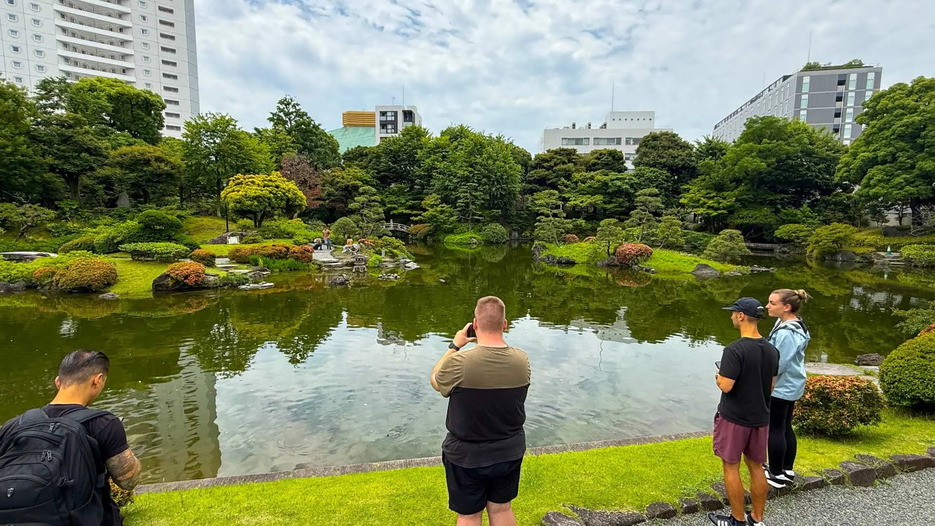 Tourists admiring a serene Japanese garden with a large pond and lush greenery in Tokyo's Ryogoku area, offering a peaceful moment amidst the bustling city.
