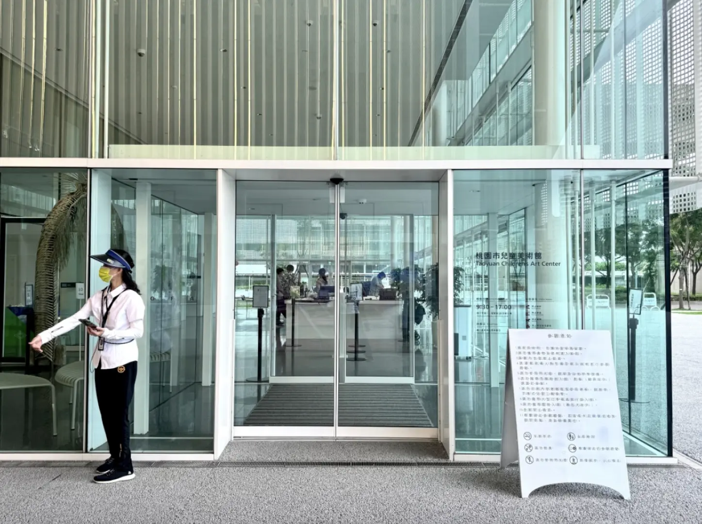 桃園市兒童美術館入口處，服務人員指引親子家庭，透明玻璃門窗營造開放舒適的藝文參觀體驗。