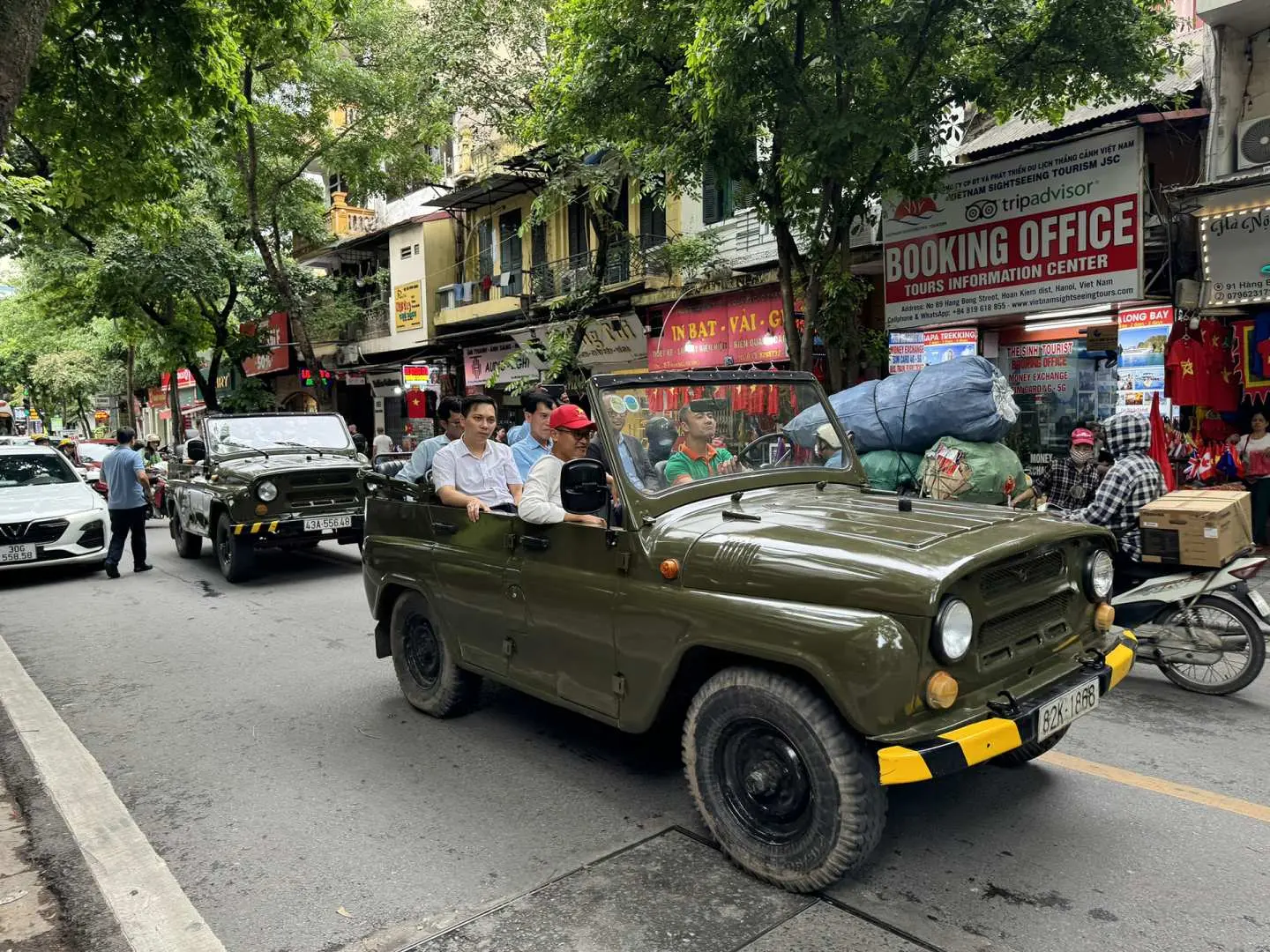 Tourists in an open UAZ Jeep drive through vibrant Hanoi streets, observing local shops and daily life.