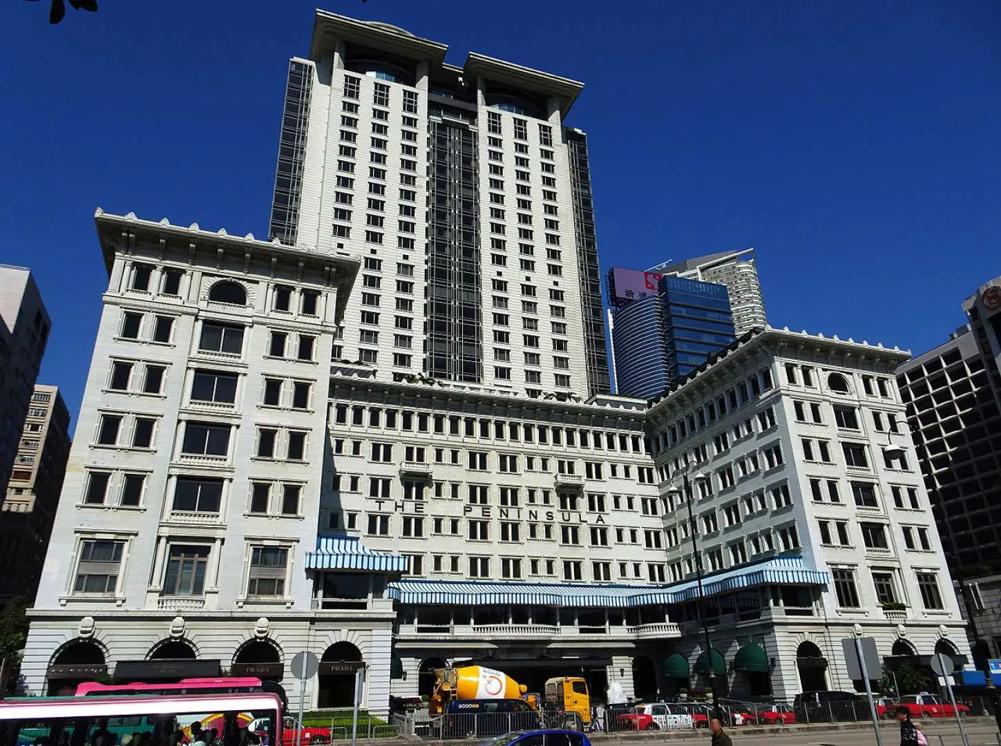 The magnificent white facade of The Peninsula Hong Kong hotel, showcasing a blend of classic colonial style with modern high-rises, a luxurious historical landmark in the city.