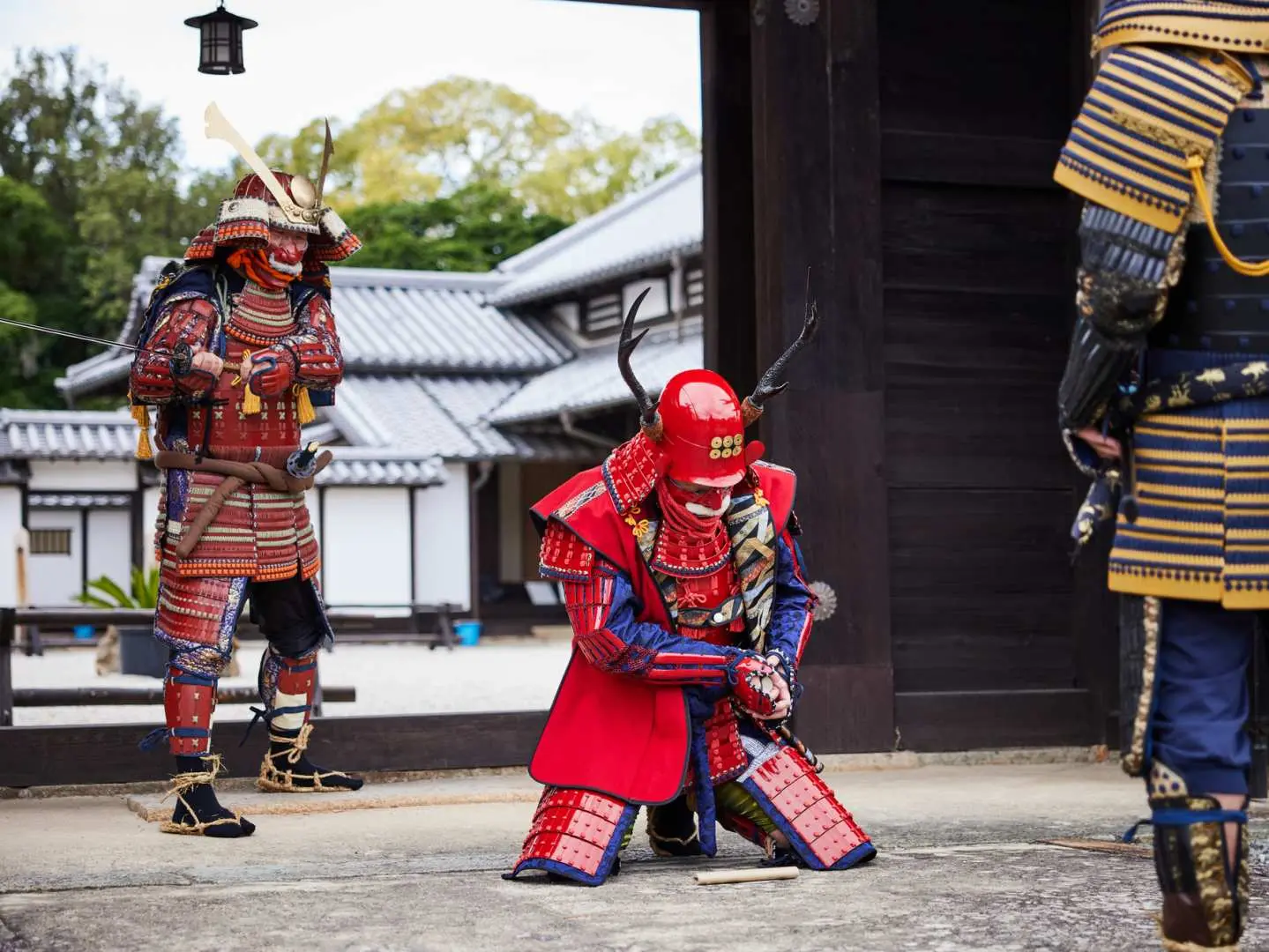 三位穿著全套武士盔甲的參與者在戶外戲劇性地擺出姿勢，一人跪地行禮，另兩人守衛，呈現戰士場景。