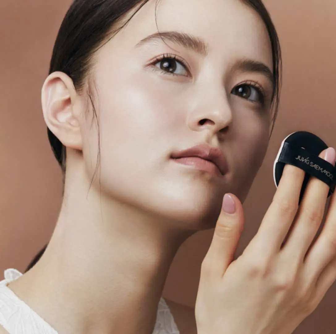 A model experiencing JUNGSAEMMOOL's professional makeup course in Seoul, using a cushion compact to create a flawless base, demonstrating the meticulousness of K-Beauty skincare and makeup services.
