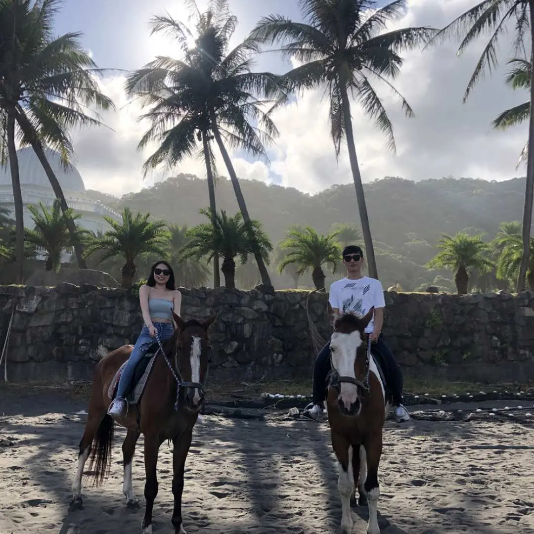 Yilan Wai'ao Little Hill Horse Farm mountain trail riding. A couple, accompanied by a professional coach, rides horses through a lush palm grove, enjoying a romantic time.