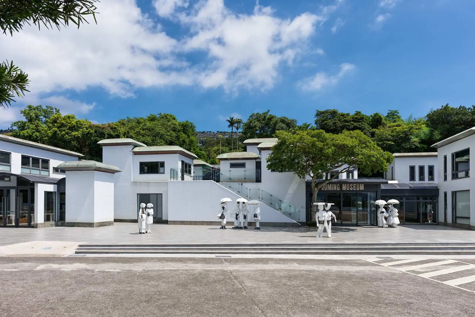 朱銘美術館潔白現代化的入口建築，戶外雕塑與綠意盎然的景觀相映襯，在藍天白雲下迎接訪客，展現藝術與自然的結合。