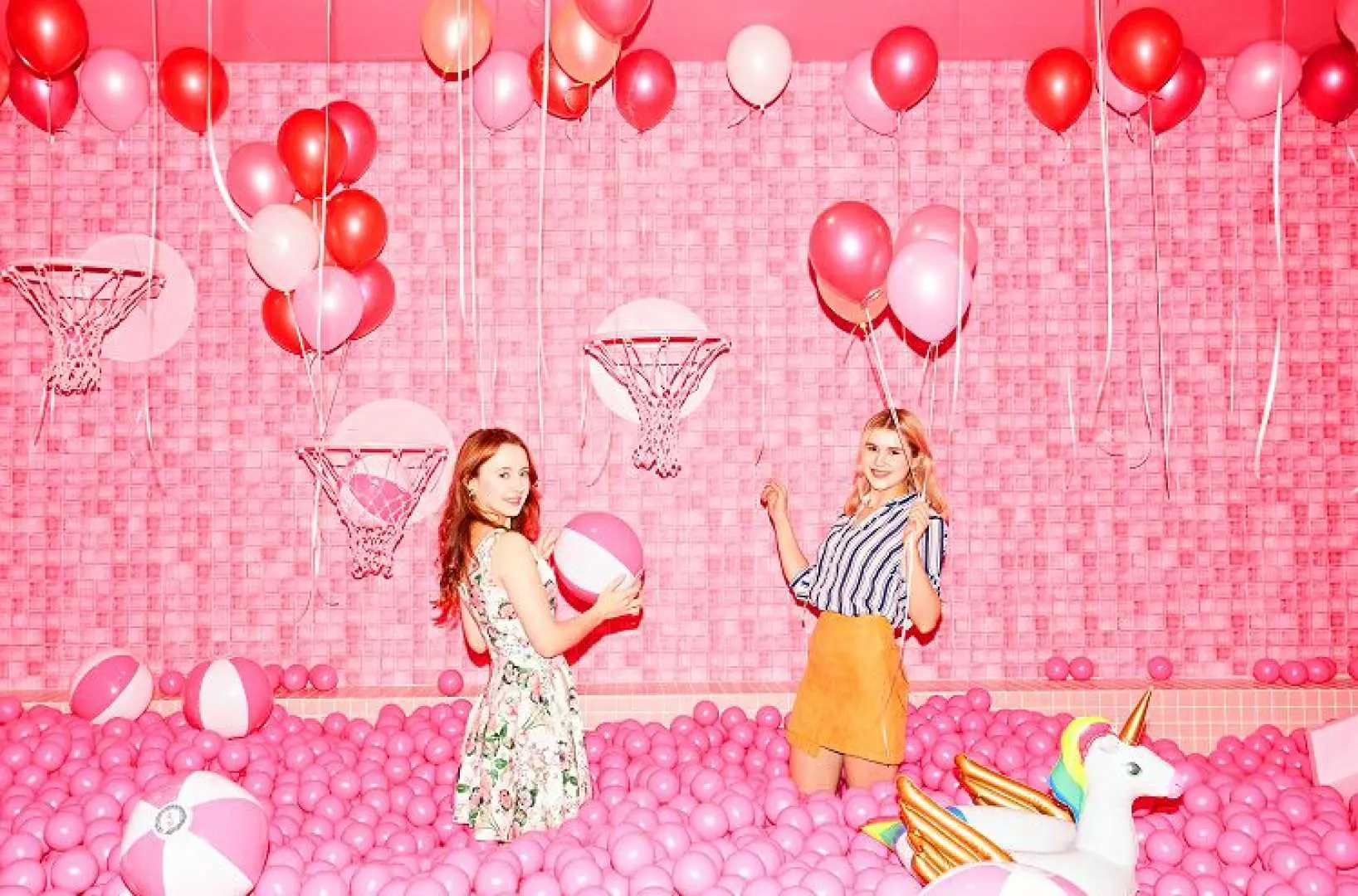 Two young women joyfully playing in the vibrant pink ball pit at Seoul's Insa-dong Color Pool Museum, surrounded by balloons and Eiffel Tower decorations, creating a dreamy photo zone.