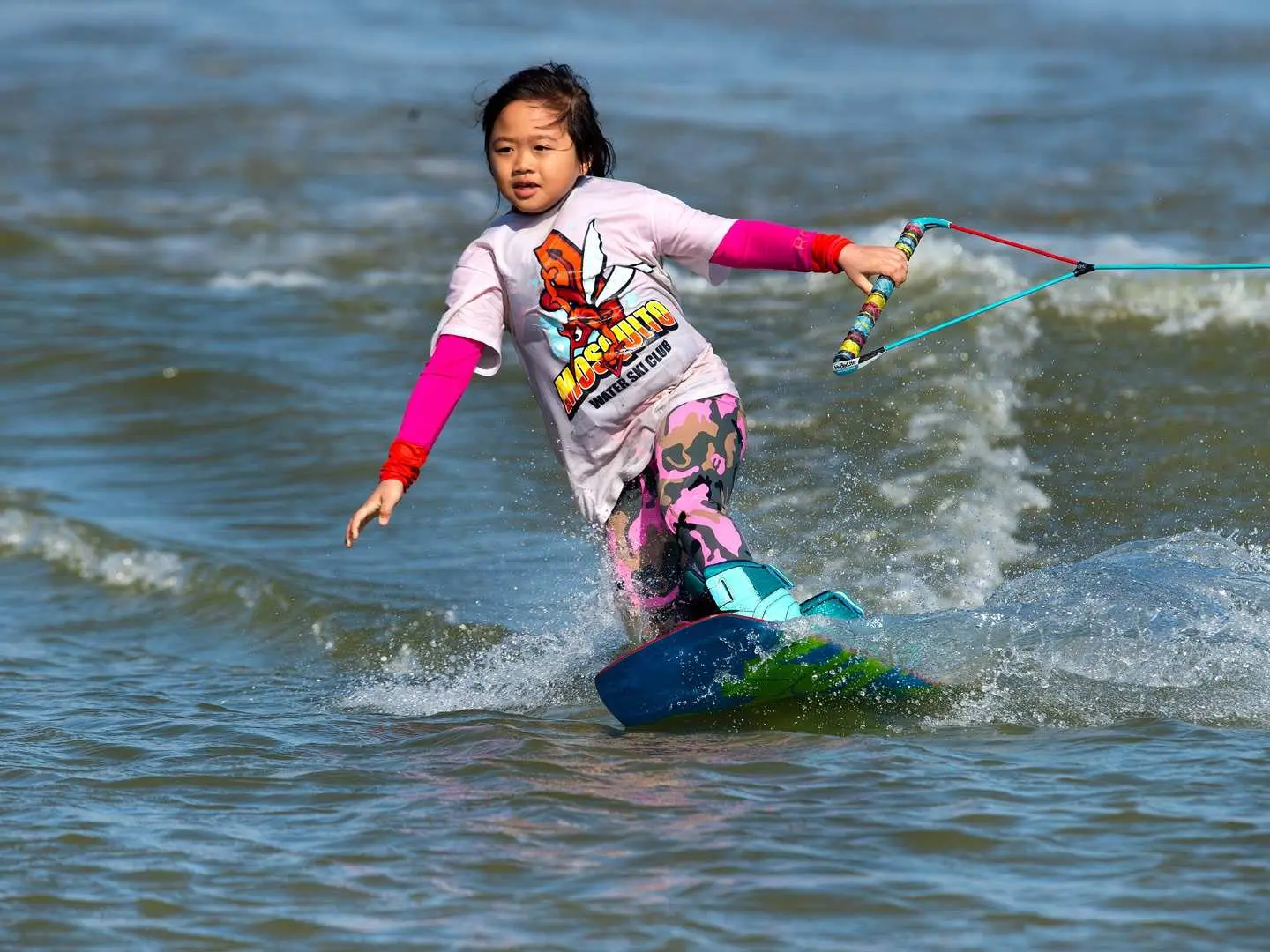 A young girl on a wakeboard at Taipei's Breeze Canal, focused on learning to glide across the water with professional guidance, illustrating this water sport is suitable for all ages.