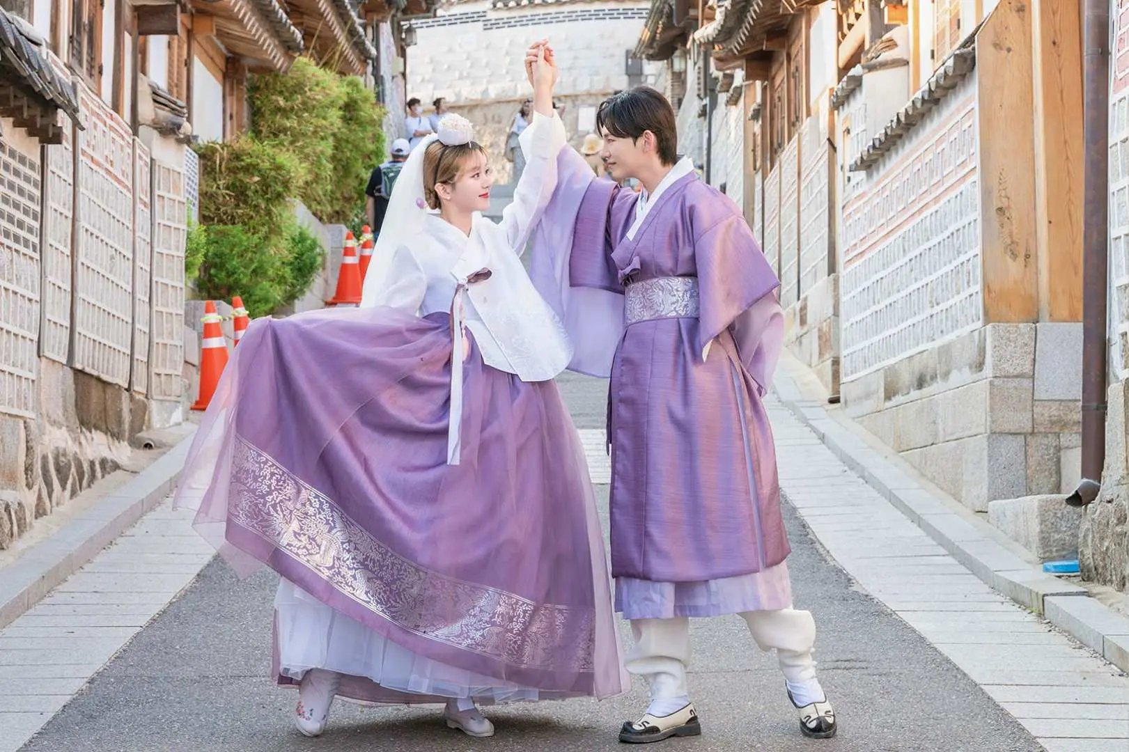A joyful couple in matching purple Hanboks playfully interacting on a charming traditional Korean street in Seoul, perfect for a romantic Hanbok photoshoot experience.
