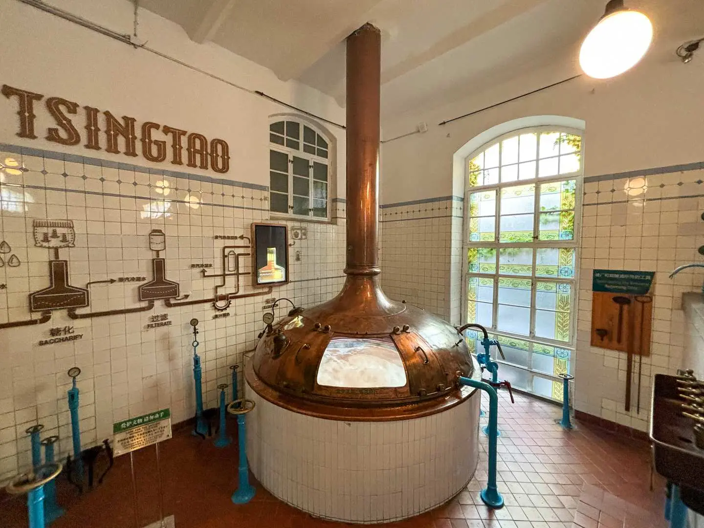 Brewing section of Qingdao Beer Museum, showcasing a colossal copper fermentation tank alongside historical diagrams on the wall, highlighting the essence and history of Tsingtao Beer's century-old craft.