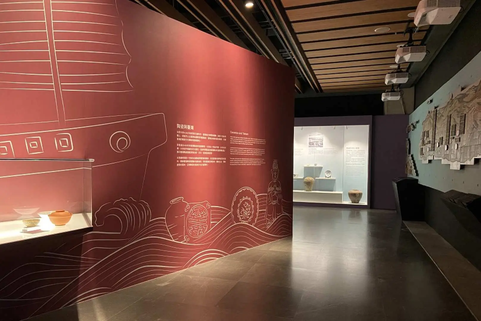 Inside the Yingge Ceramics Museum exhibition hall, a vibrant red feature wall with sailing and pottery motifs, complementing displays of exquisite ceramic artifacts.