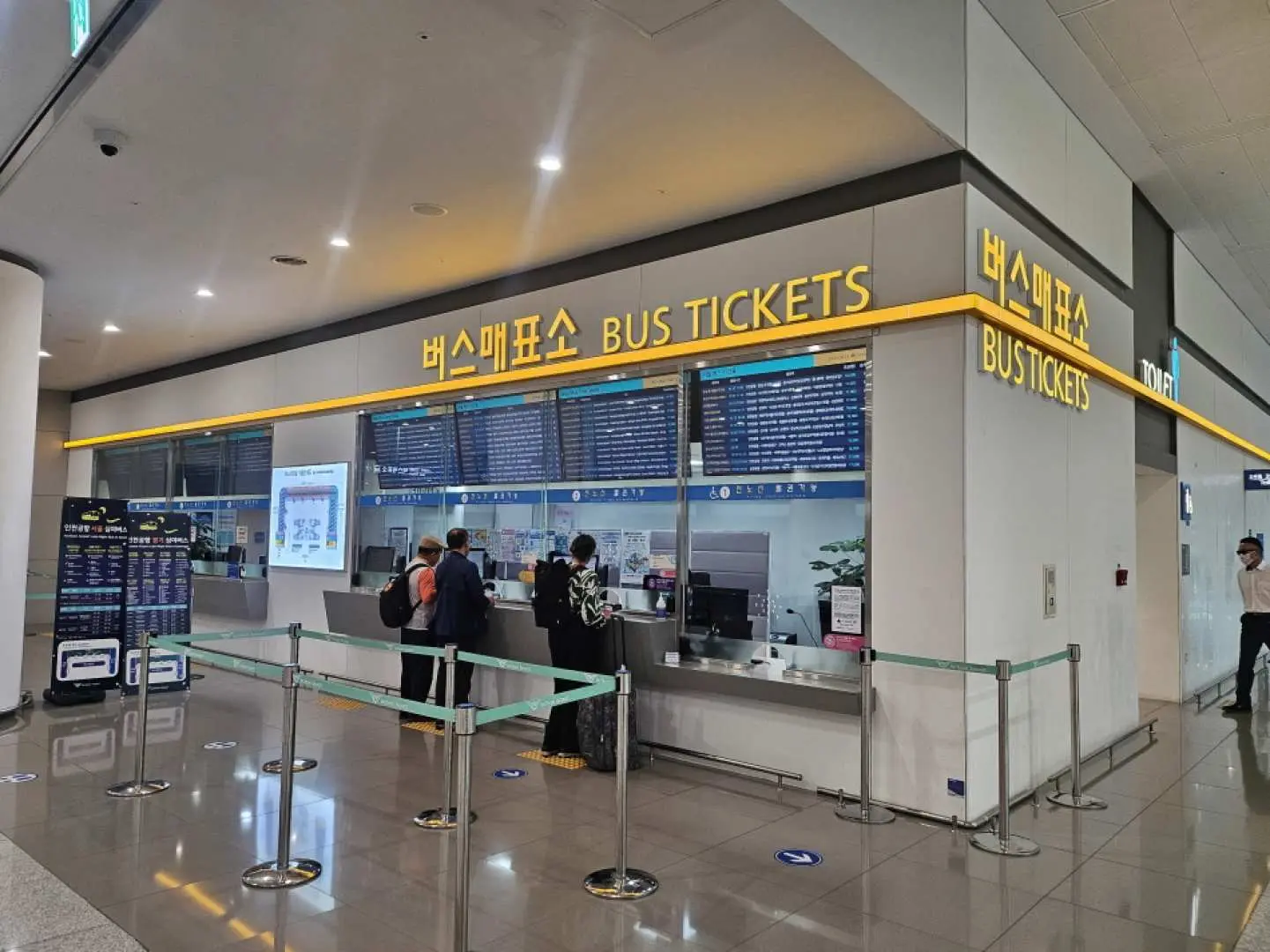 An airport bus ticket counter inside Incheon International Airport, with travelers queuing to purchase tickets for the 6100 luxury bus service.