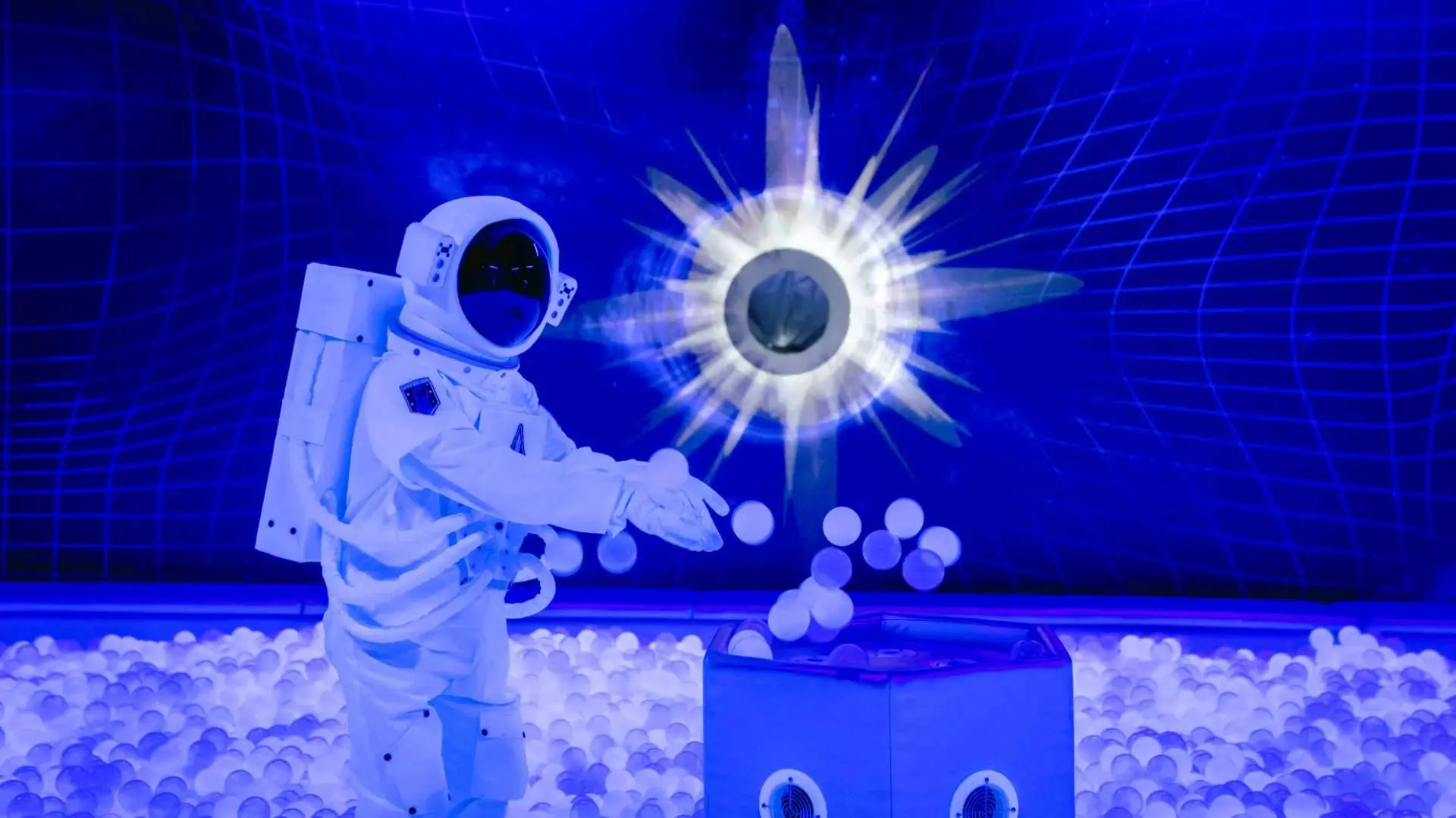 Astronaut figure in a blue-lit interactive exhibit at Guangzhou Zhengjia Planetarium, surrounded by white balls and a glowing celestial object, creating an immersive space experience.