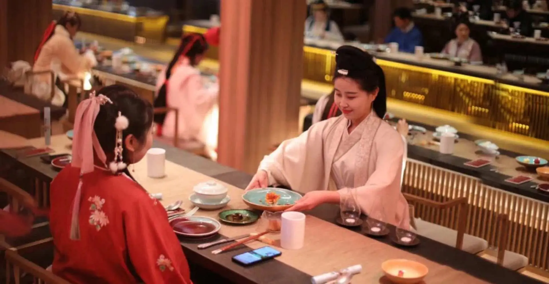 At Beijing Palace Banquet, a 'palace maid' in Hanfu respectfully serves dishes with imperial etiquette to a guest in period costume, offering an immersive role-playing dining experience.
