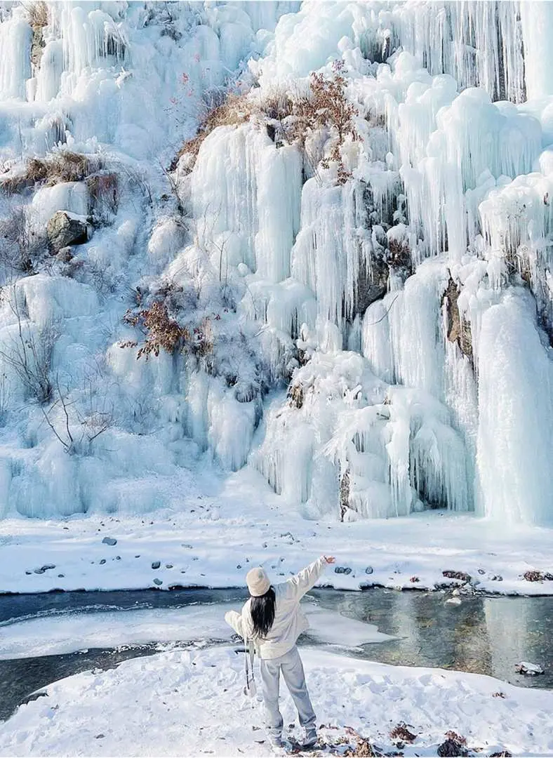 一位遊客在艾奧比山谷冰瀑前雪地中歡快地張開雙臂，享受韓國冬季自然美景，是首爾出發一日遊的難忘體驗。