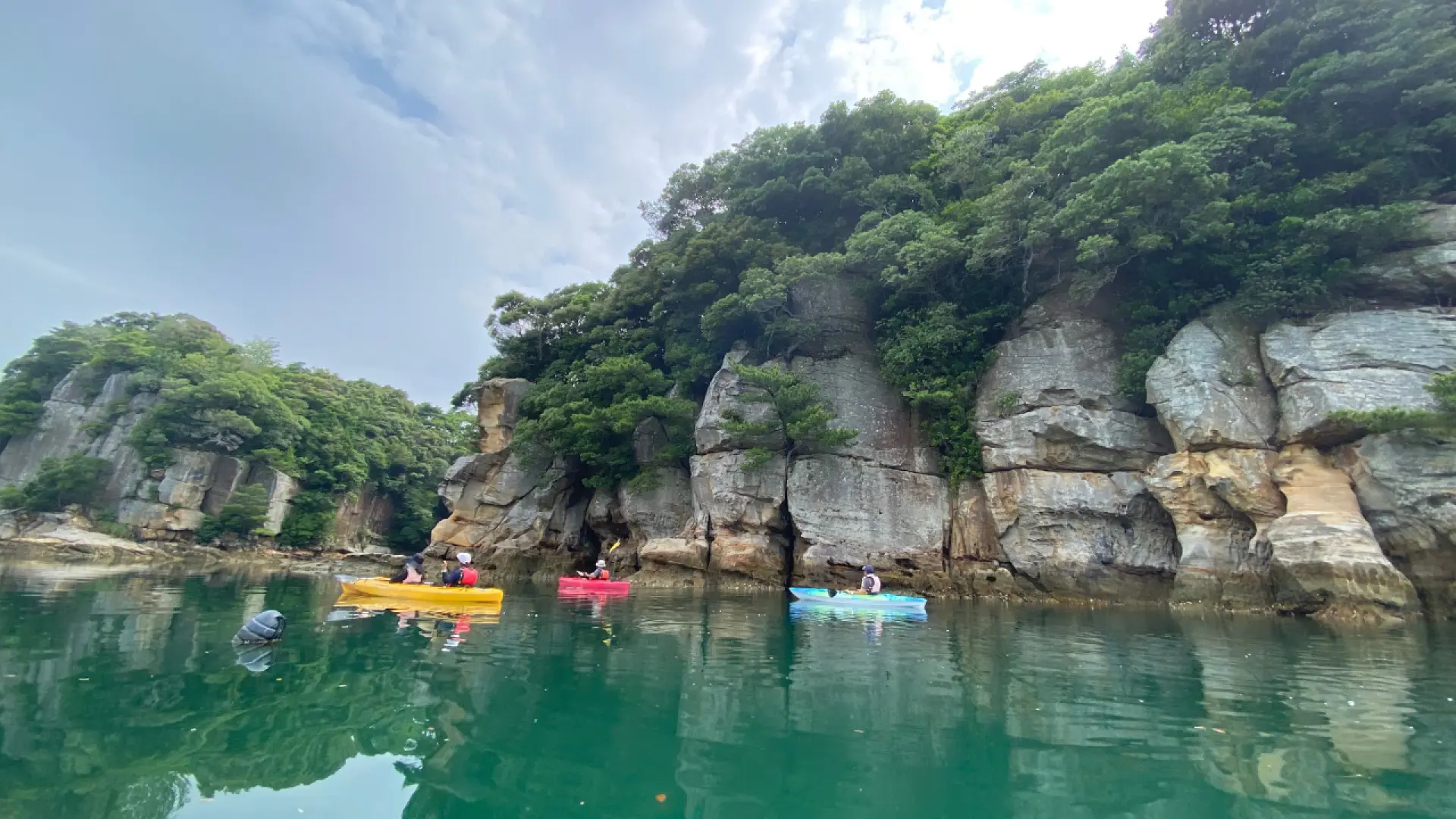 九十九島獨木舟體驗，數艘皮划艇沿著壯觀的海岸線航行，周圍環繞著綠意盎然的島嶼和雄偉岩壁。