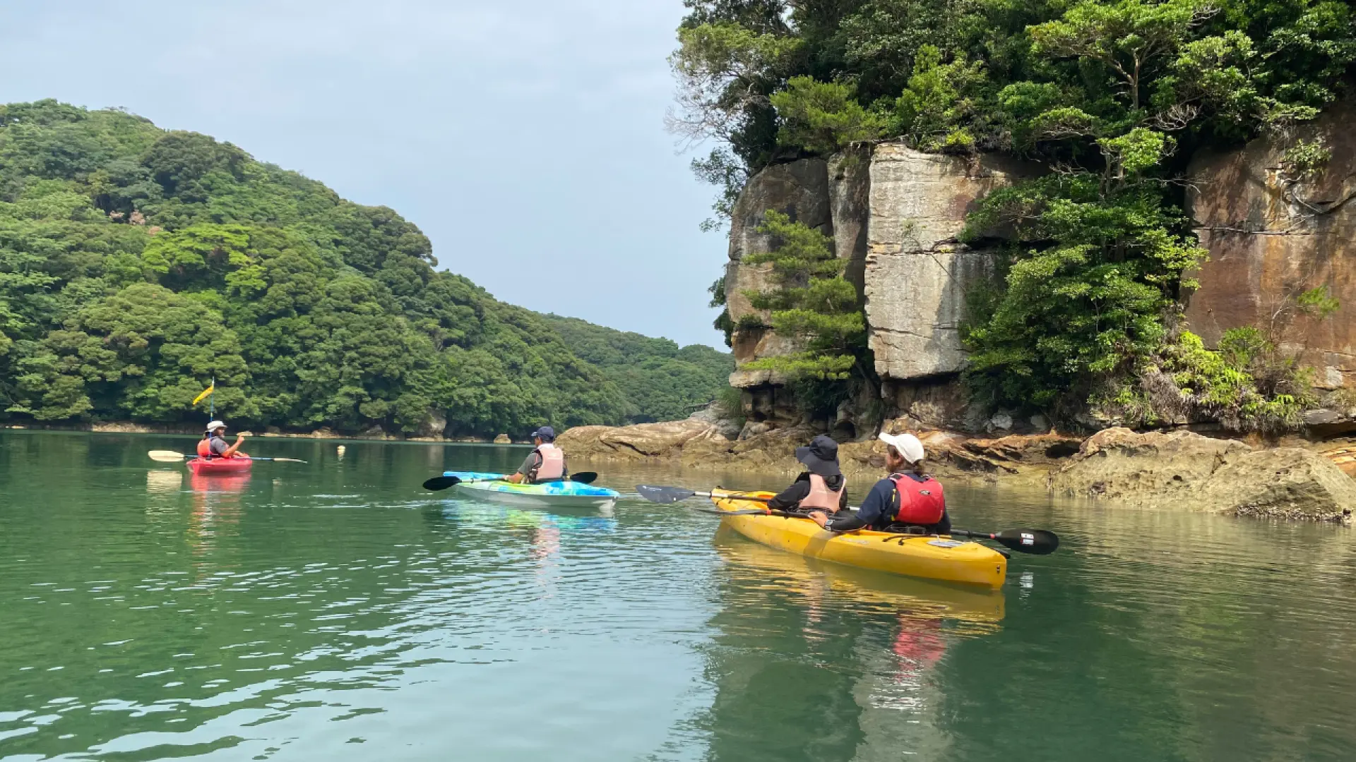 西海國立公園九十九島，獨木舟團體悠閒地劃過平靜海面，探索翠綠島嶼與獨特岩層。