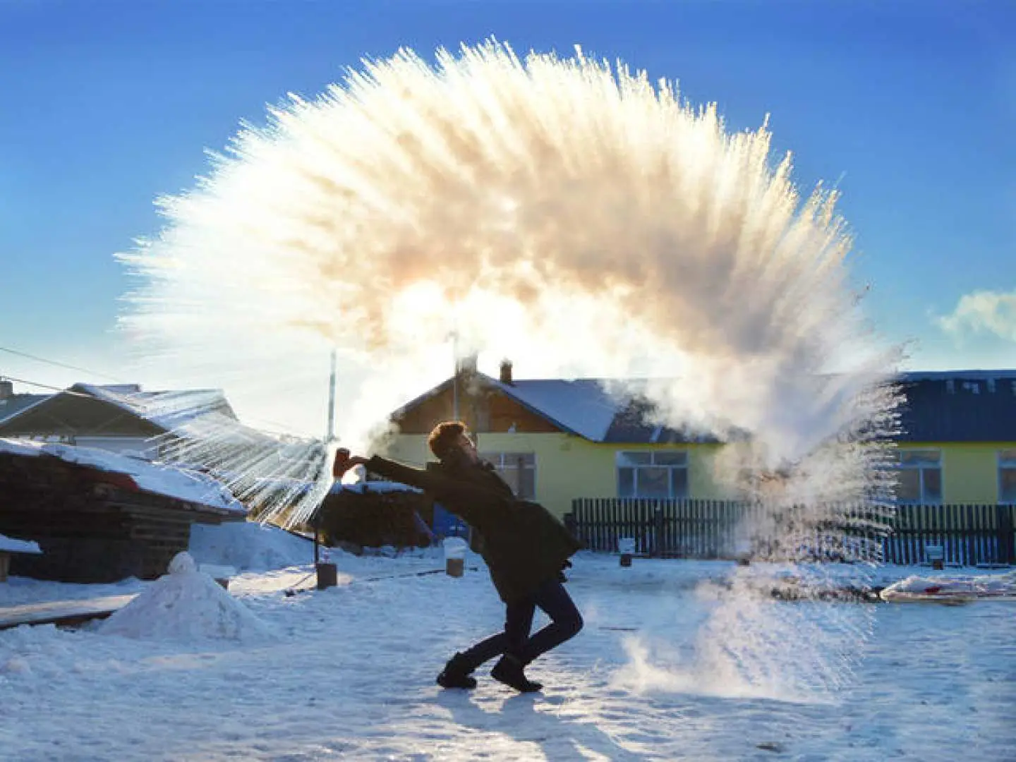 游客在哈尔滨雪乡体验泼水成冰的趣味冬季活动，阳光下水雾瞬间凝结成冰，享受独特的冰雪乐趣。