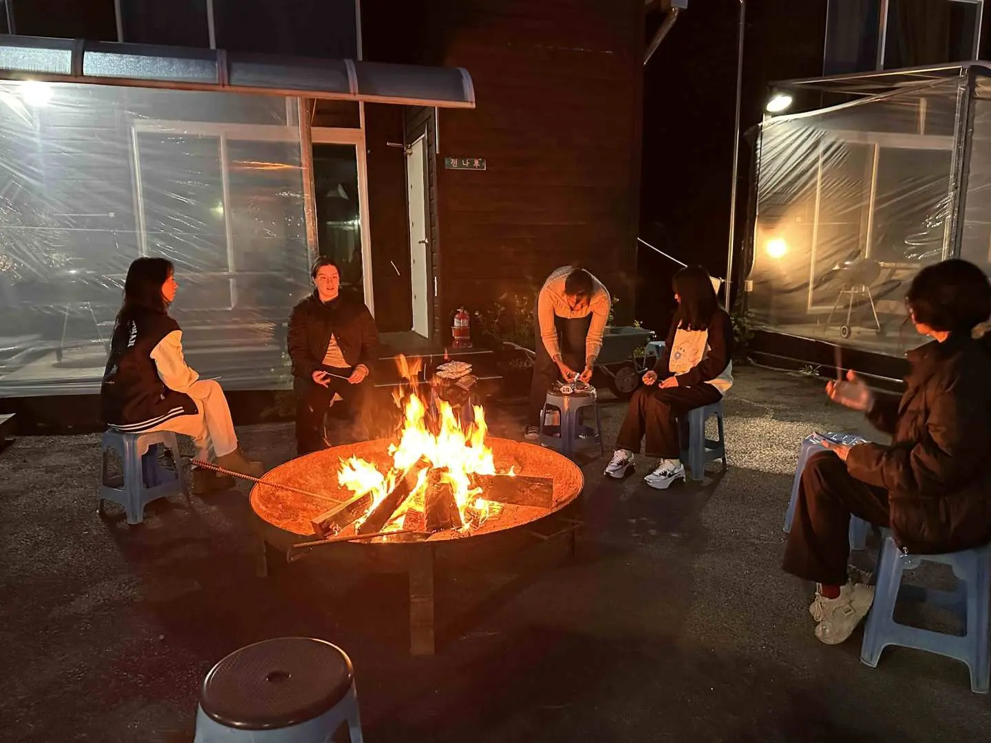 国际旅客夜晚围着大型温暖篝火，享受韩式MT体验中的社交与放松篝火晚会。