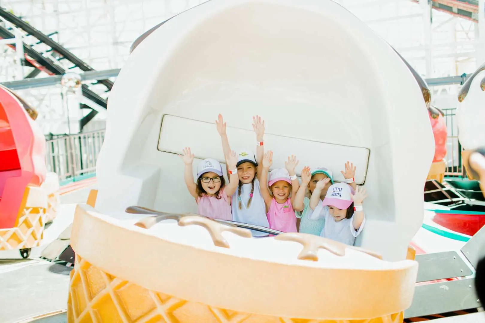 Several children gleefully riding an ice cream-shaped spinning attraction at a San Diego theme park, raising their hands in joy, embracing childhood fun.