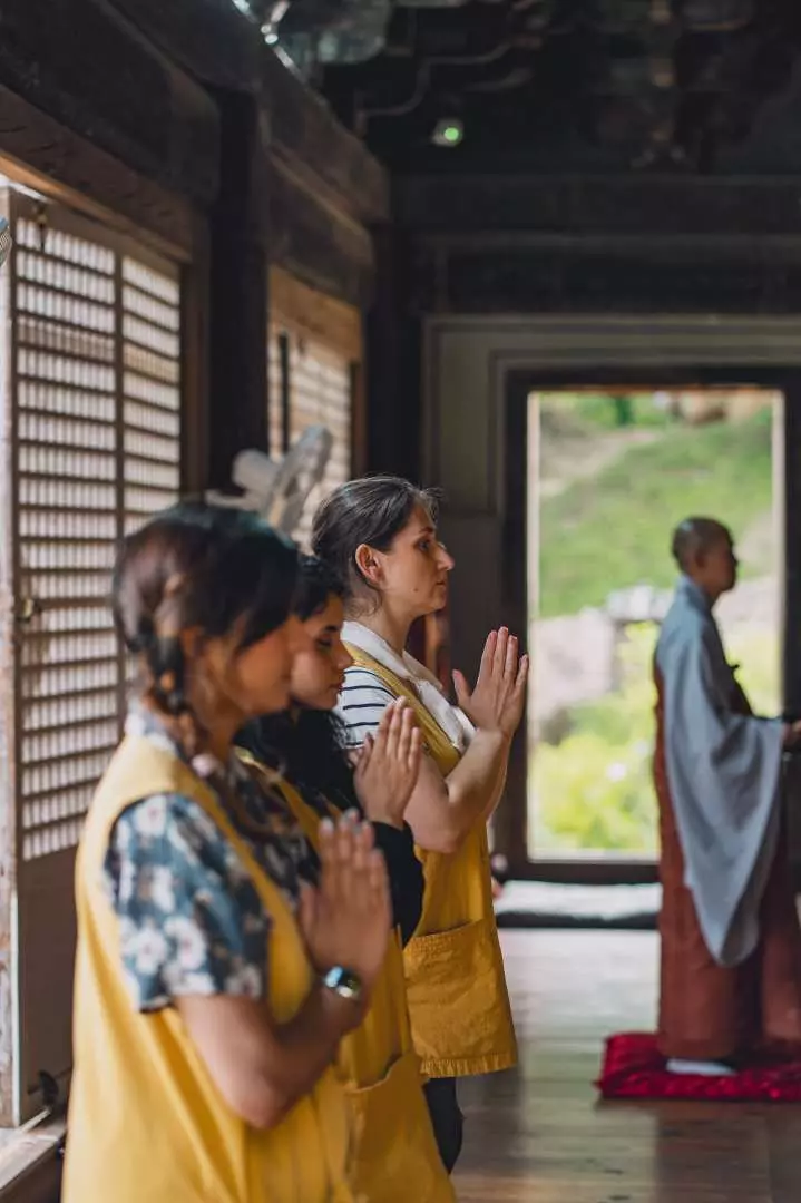 Multiple participants and a monk engaged in a Buddhist service or meditation inside Bongjeongsa Temple, hands pressed together, experiencing the spiritual tranquility and immersive reflection of the temple stay.