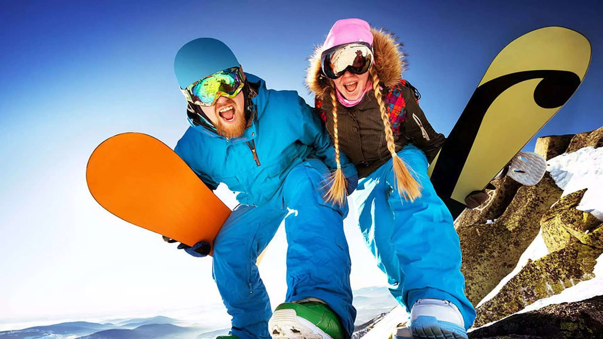 Two cheerful young snowboarders, a man and a woman, holding snowboards and smiling widely against a bright sky, enjoying winter sports at Beijing's Nanshan Ski Resort.