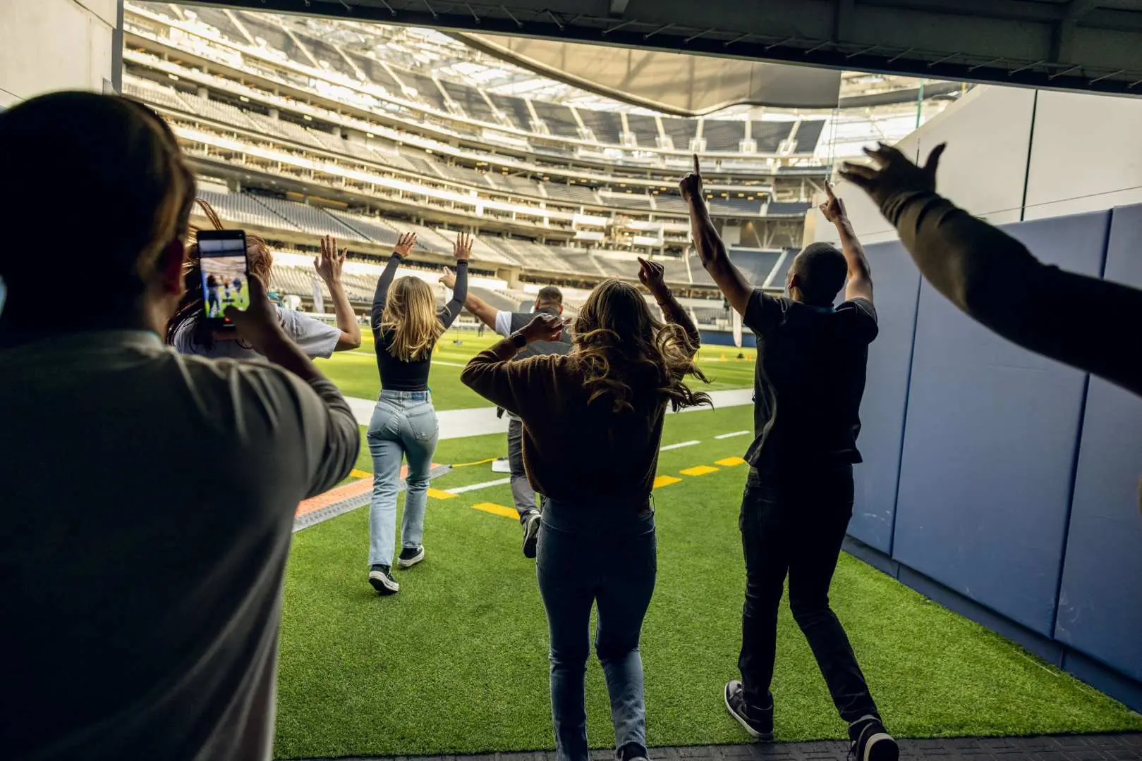Visitors enthusiastically running onto the vast field during a SoFi Stadium tour in Los Angeles, experiencing the thrill of a world-class sports arena.