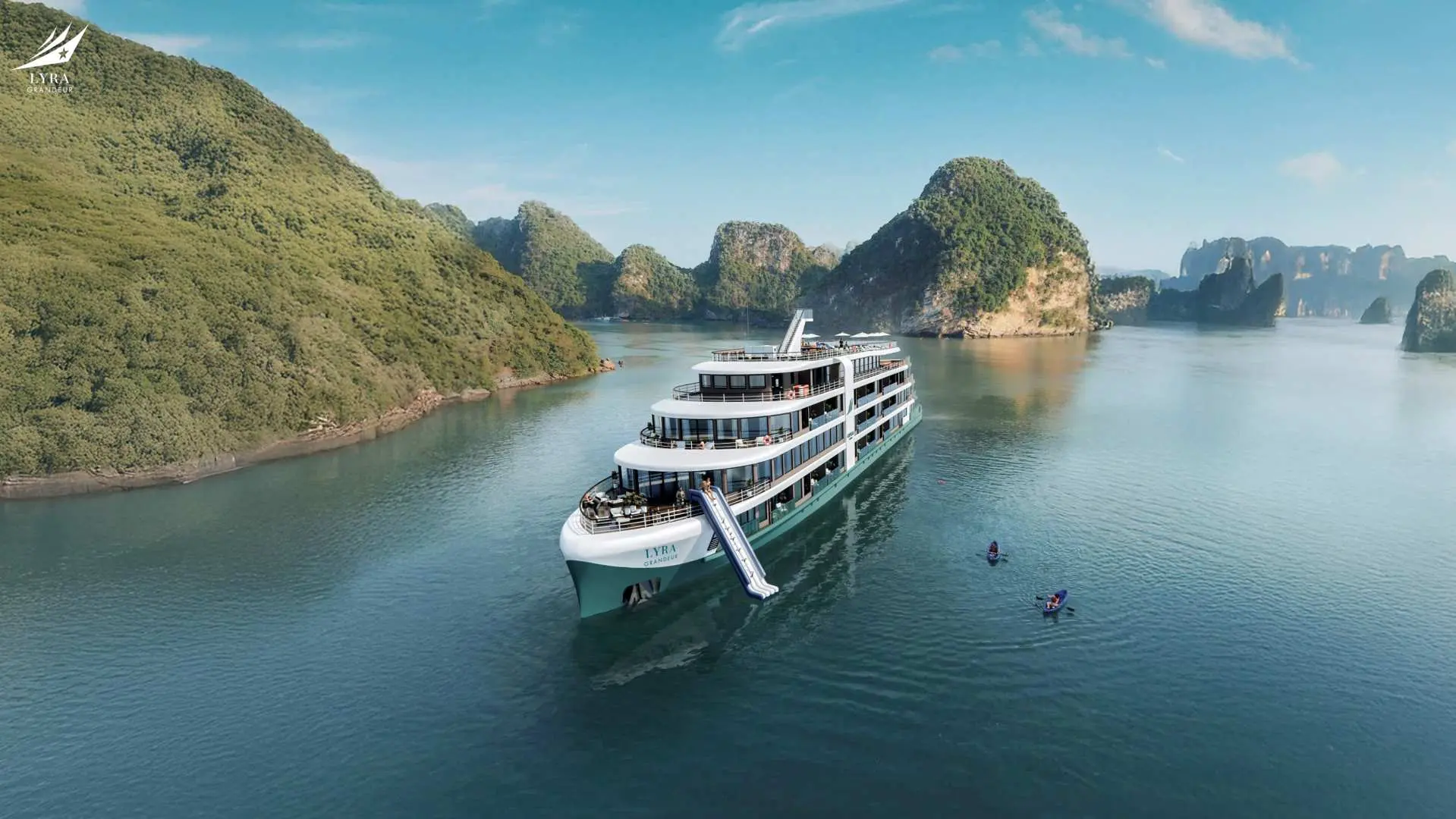 An aerial view of the Lyra Grandeur luxury 6-star cruise gracefully sailing through Vietnam's Lan Ha Bay, surrounded by iconic limestone islands, with kayakers nearby.