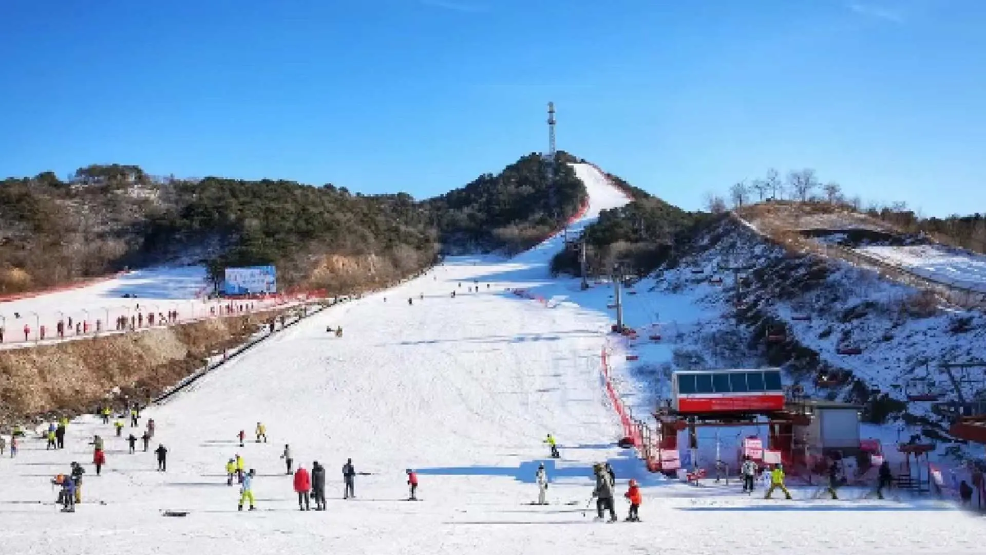 北京云佛山滑雪场的开阔雪道上，众多滑雪爱好者与初学者享受冬季运动，远处可见缆车及山顶信号塔，尽情体验畅滑乐趣。