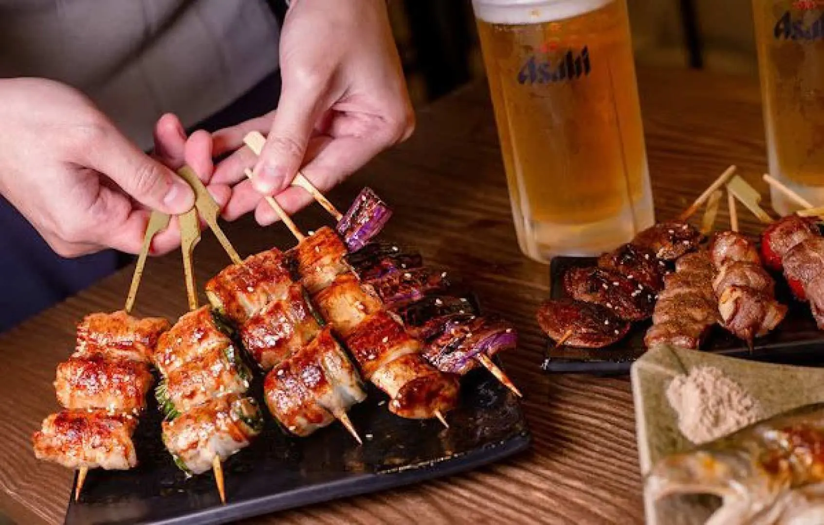 Charcoal-grilled Japanese skewers and a craft beer on a table at GULUGULU playful bar, offering a delicious two-person set meal experience in Tsim Sha Tsui.