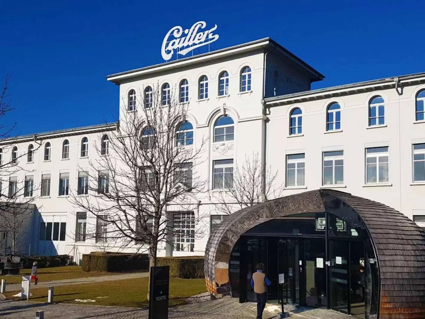 瑞士最古老的Maison Cailler巧克力工廠雄偉的白色建築外觀，擁有獨特木質拱門入口，在藍天下顯得格外引人注目。