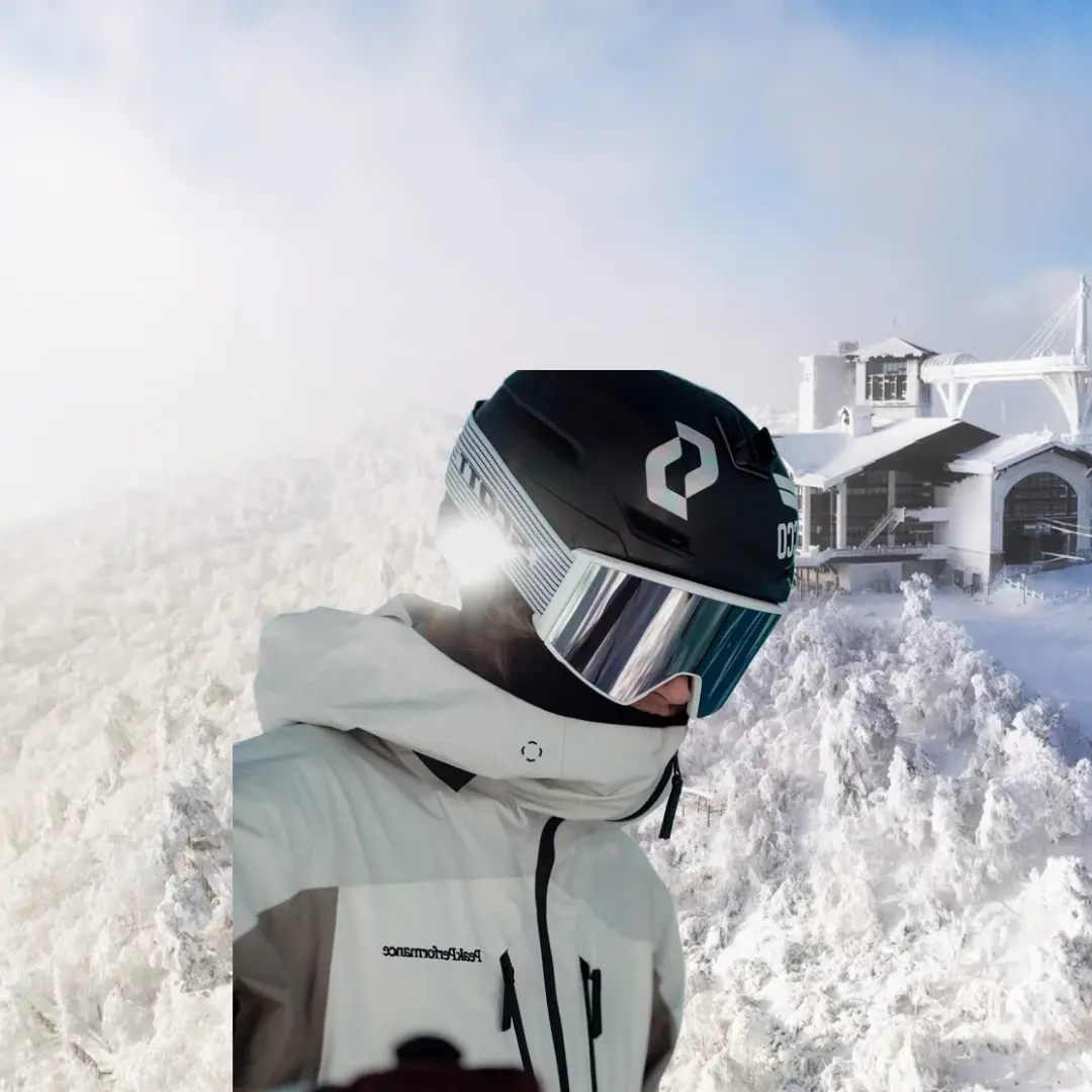 Close-up of a skier in helmet and goggles, with the snowy slopes and resort buildings of Yongpyong Ski Resort blurred in the background.
