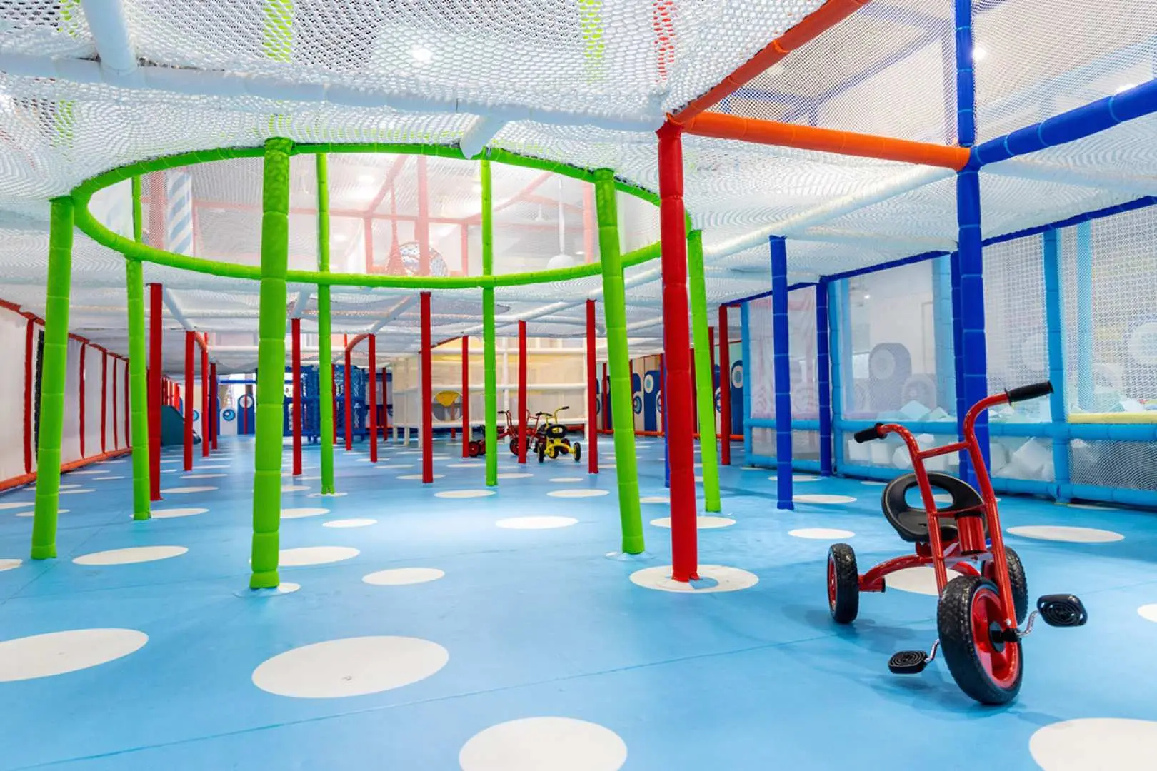 Spacious indoor facility at New Taipei POPA Parent-Child Physical Activity Center, featuring a blue floor with white polka dots, colorful pillars, and several children's tricycles for toddlers to safely learn riding.