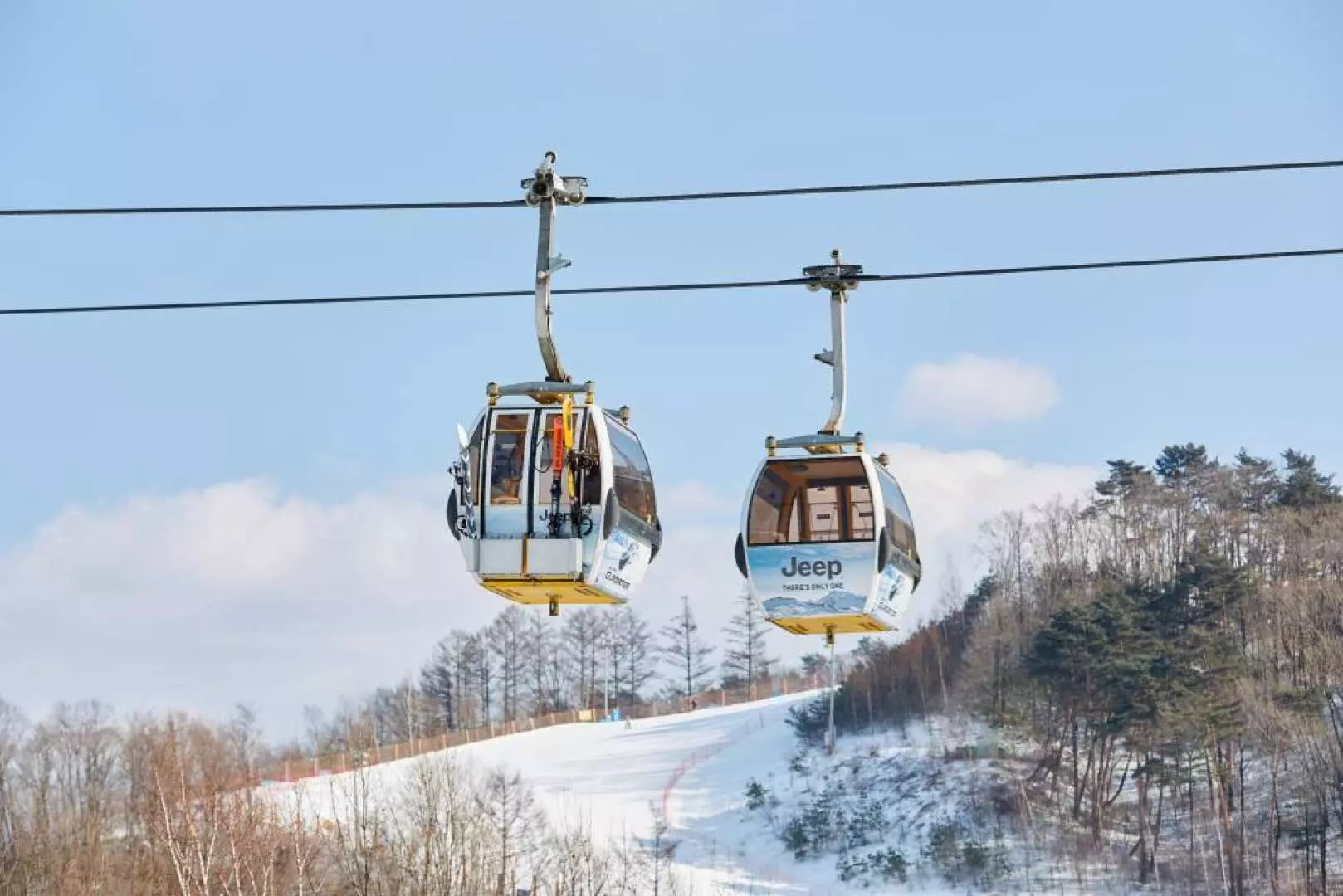 平昌鳳凰雪上樂園的纜車在晴朗藍天下滑行，遊客可從高空俯瞰白雪皚皚的山坡與樹林，享受壯麗雪景。