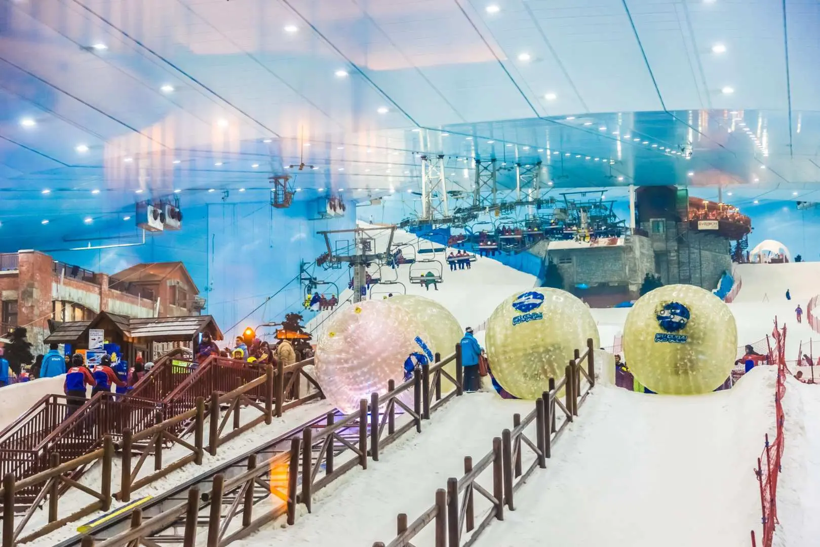 Adventurous visitors engaging in exciting zorbing on the snow slopes at Ski Dubai's Snow Park, with unique winter village scenery and various snow play activities in the background.