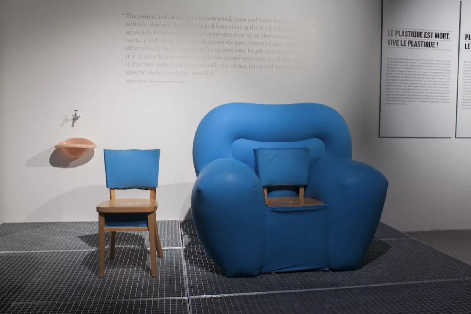 Modern design exhibits inside Brussels' Atomium, featuring a blue inflatable art chair beside a wooden chair, with wall slogans adding cultural context to the unique display.